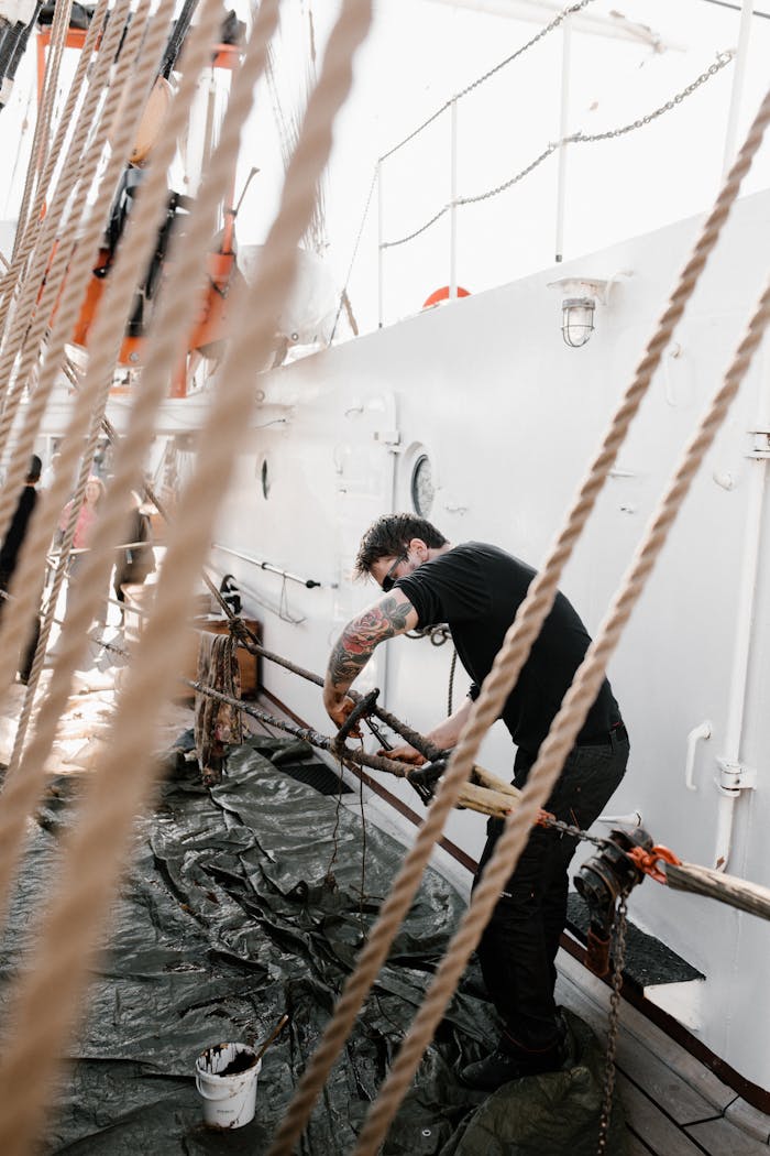 A tattooed sailor manages ropes on a well-bound ship under sunlight, showcasing seamanship.